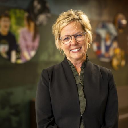 A white woman with blonde hair and glasses, wearing a suit jacket and skirt.