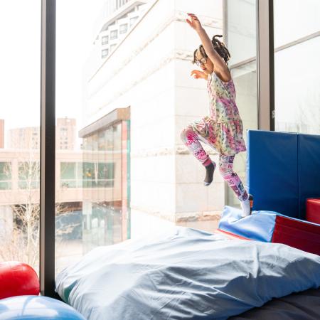 A little girl with braids leaping onto a soft crash pad in an OT gym.