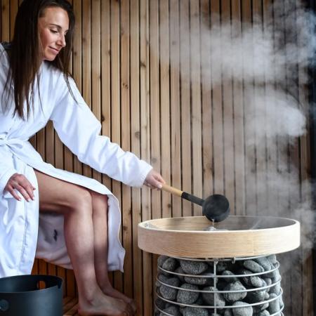 woman in sauna pouring water on stones