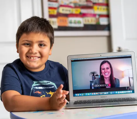 A child smiling next to a laptop screen