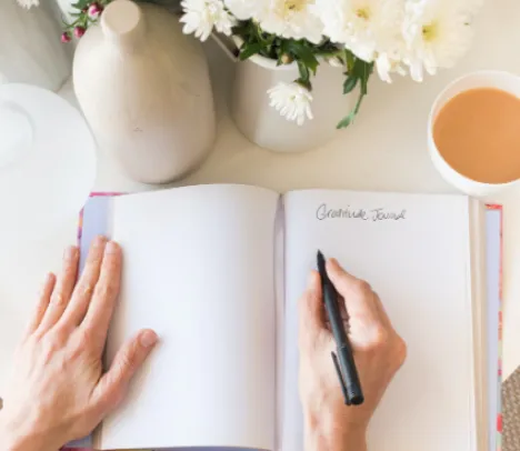 A person writing in a journal at a table with coffee