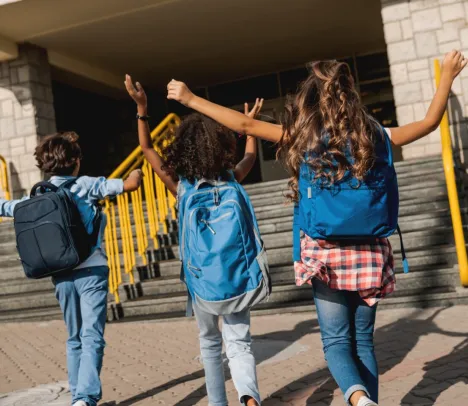 The backs of three school-aged children excitedly walking into school