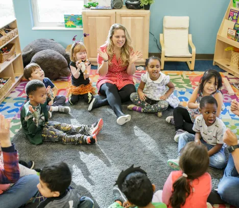 preschool children and teachers seated in a circle and smiling