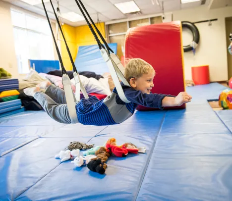 child swinging in a colorful occupational therapy gym