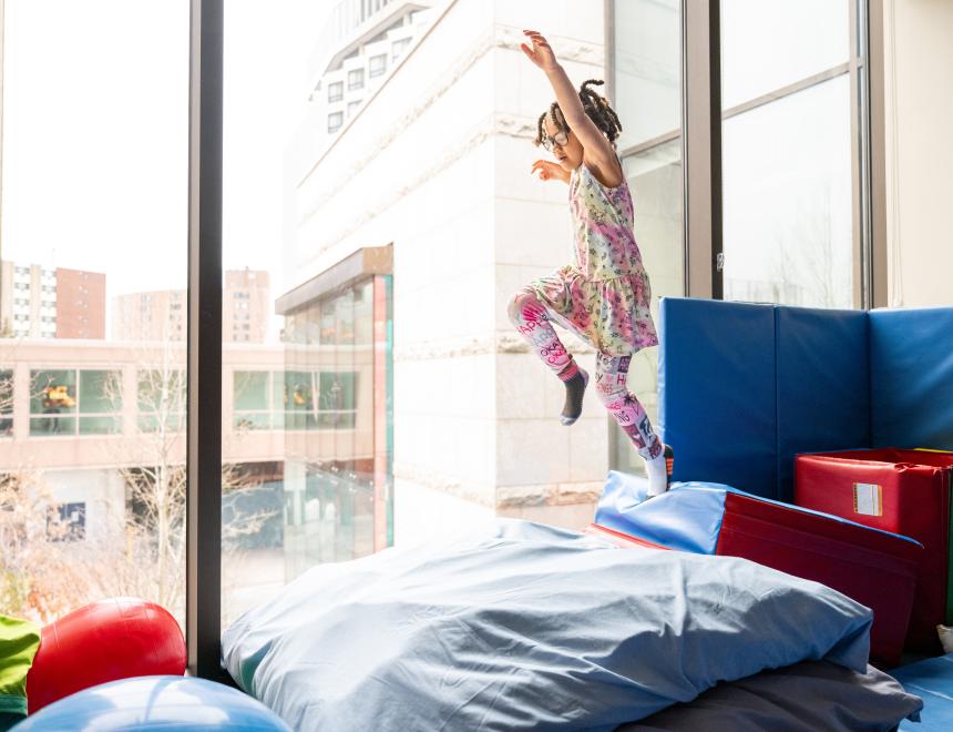 A little girl with braids leaping onto a soft crash pad in an OT gym.