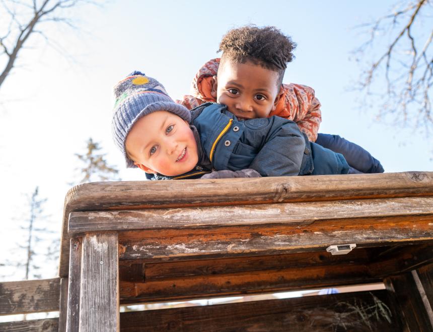 Two preschool boys play together on top of a bench.