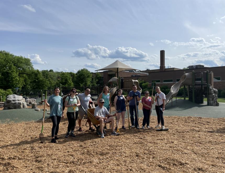 Group of adults standing on a playground with shovels and wheelbarrows after spreading new mulch.