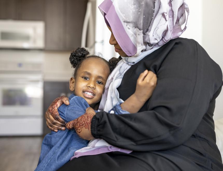 Dark-skinned mother wearing a hijab hugging daughter with hair buns.