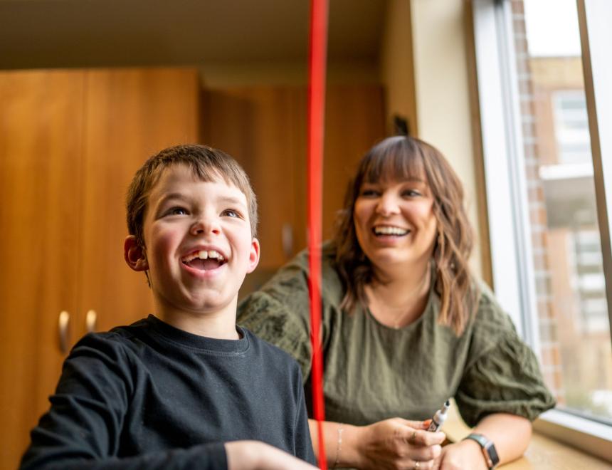 Little boy with short brown hair and a female therapist with long brown hair play with a ribbon by a window.