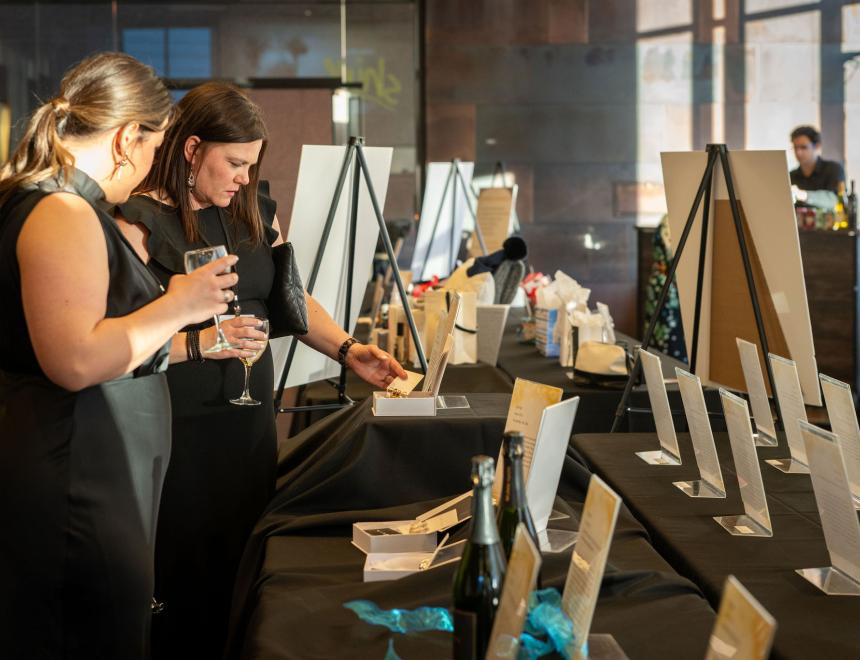 people looking at auction items on tables with black linens
