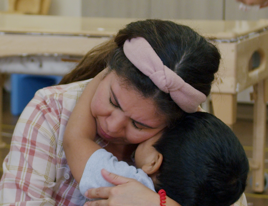 Child hugging teacher in classroom. 
