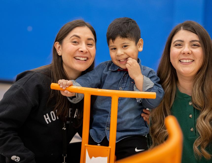 Two therapists on either side of a little boy, playing on a tricycle.