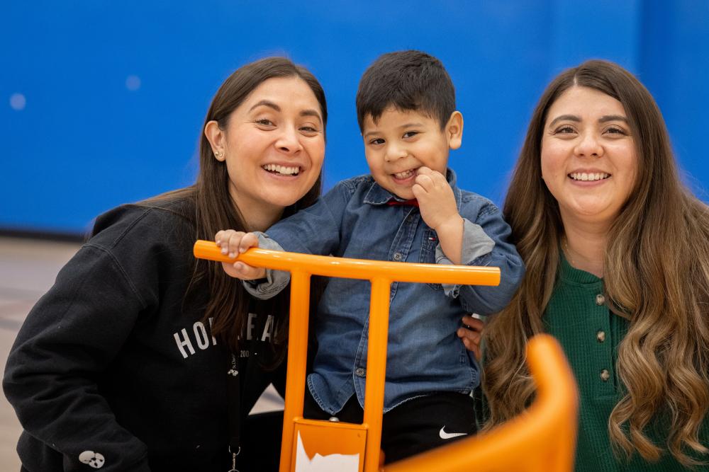 Two therapists on either side of a little boy, playing on a tricycle.