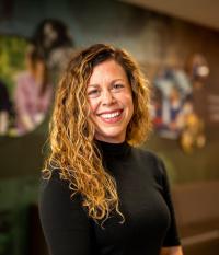 White woman with curly light brown hair, wearing a black long-sleeved top, smiling.