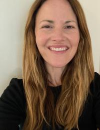 White woman with long dark blond hair, wearing a black top, smiling.