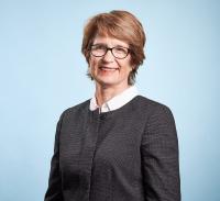 White woman with short brown hair and glasses, wearing a dark top.