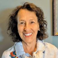 Smiling woman with brown curly hair, wearing a light-colored top.