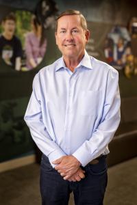 While male in light colored button-up shirt, smiling. 