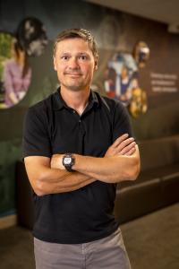 White man wearing a black polo shirt, with arms crossed. 