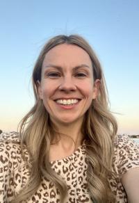 Smiling woman with long blonde hair with a blue sky behind her.