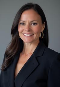 White woman with long brown hair, wearing a suit coat and smiling.