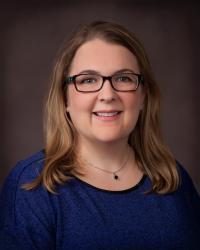 White woman with shoulder-length light brown hair and glasses, smiling.