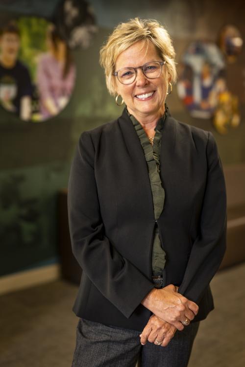 A white woman with blonde hair and glasses, wearing a suit jacket and skirt.