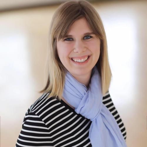 White woman with dark blonde hair, light blue scarf and striped shirt. 