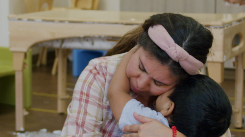 Child hugging teacher in classroom. 