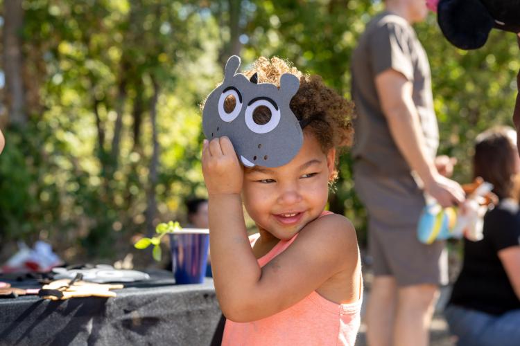 Little girl lifting an animal mask above her eyes, smiling.