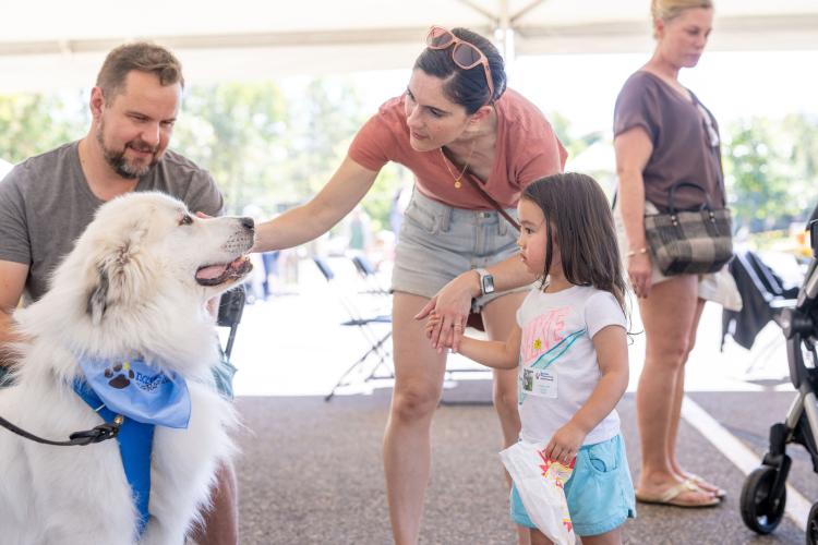 Little girl and her caregivers petting a big white fluffy therapy dog.