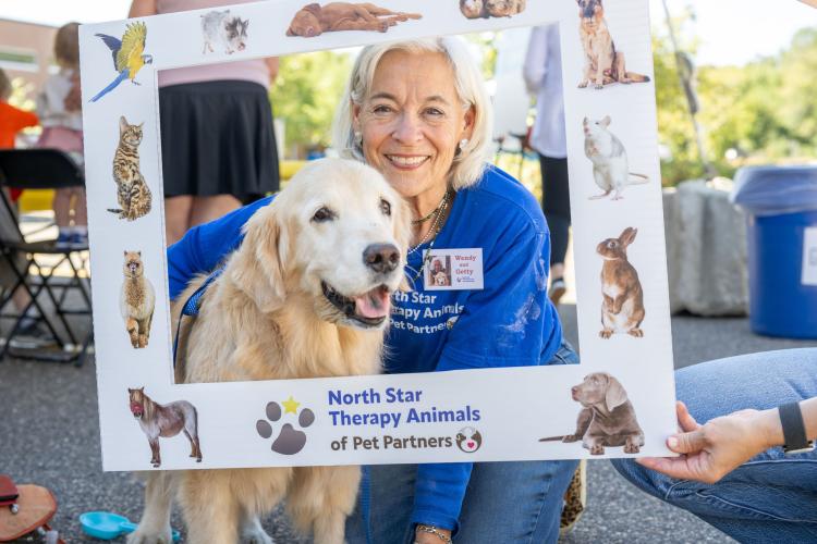 Older woman and her golden retriever holding up a big photo frame.