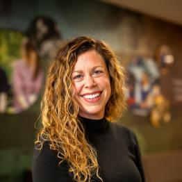 White woman with curly light brown hair, wearing a black long-sleeved top, smiling.