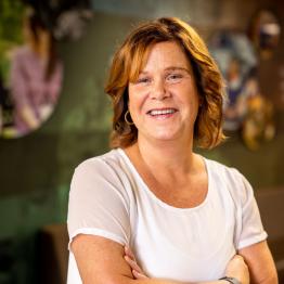 white woman with shoulder-length red hair, wearing a white top, smiling at the camera.