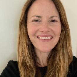 White woman with long dark blond hair, wearing a black top, smiling.