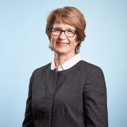 White woman with short brown hair and glasses, wearing a dark top.
