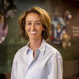 Brunette white woman wearing a button-up shirt and jeans, smiling.