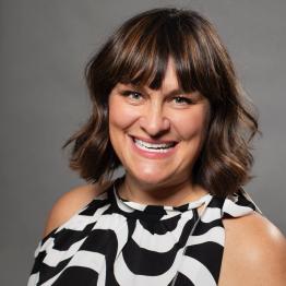 Smiling woman with brown, shoulder-length hair and bangs, wearing a black and white top.