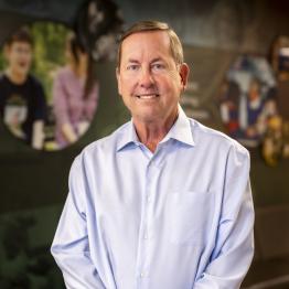 While male in light colored button-up shirt, smiling. 
