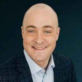 White man with no hair wearing a button-up shirt and suit jacket, smiling.