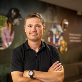 White man wearing a black polo shirt, with arms crossed. 