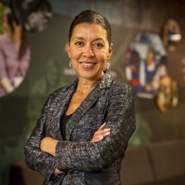 Woman with tan skin and pulled back dark hair, wearing a suit jacket and skirt, smiling.