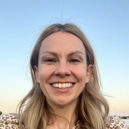 Smiling woman with long blonde hair with a blue sky behind her.
