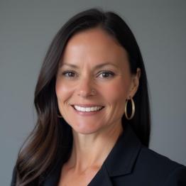 White woman with long brown hair, wearing a suit coat and smiling.