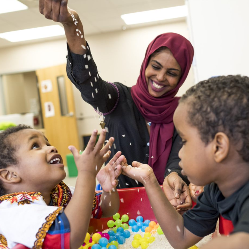 Two East African therapists and two students joyfully play around a sensory table.