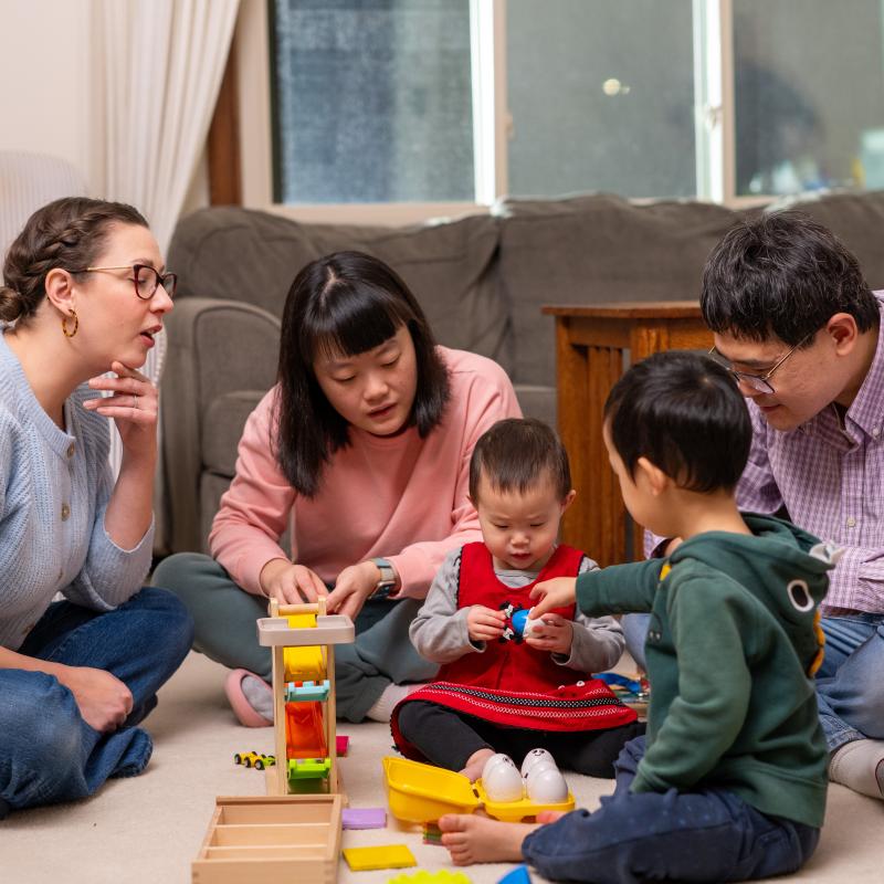 A therapist, mother, father, and two young children play on the floor of a living room. 
