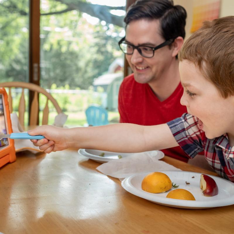A child at a dining table interacting with a tablet