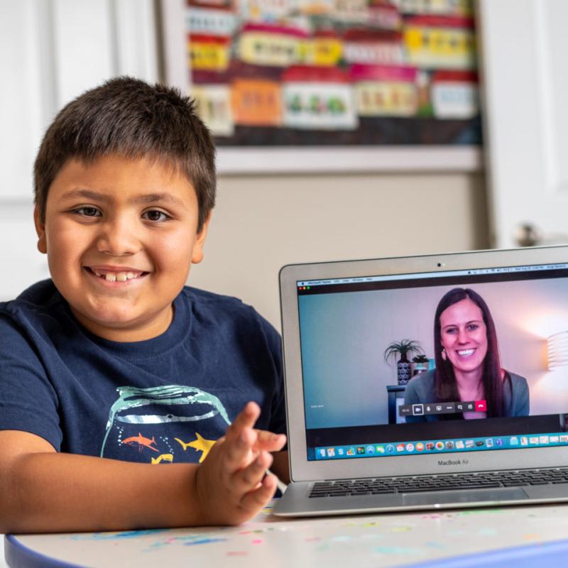 A child smiling next to a laptop screen