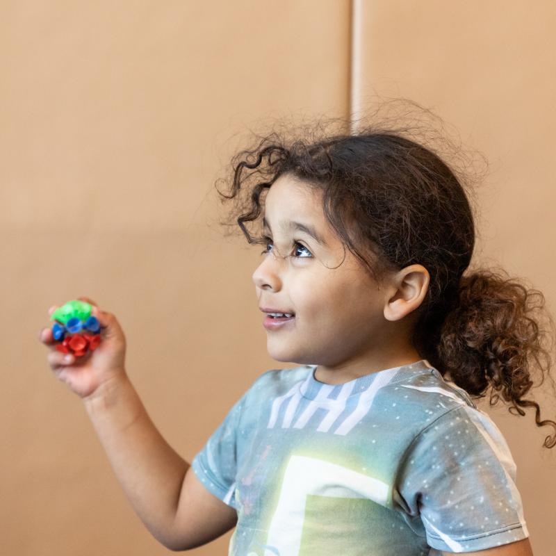 Little boy with ponytail holding a ball in an OT gym.