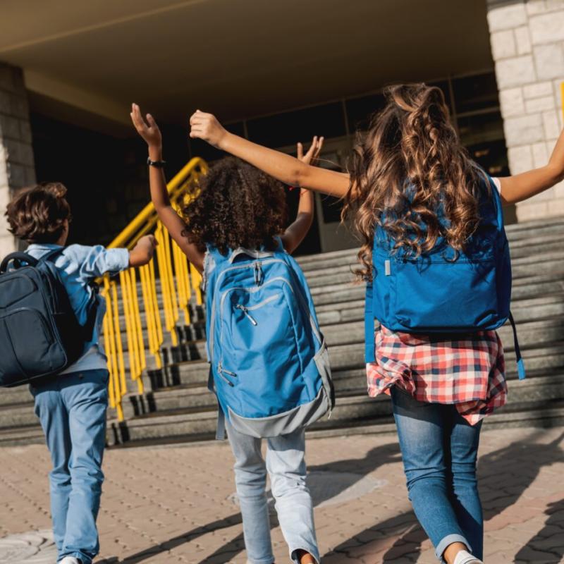 The backs of three school-aged children excitedly walking into school